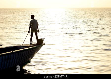 Persona sagomata a prua della barca al tramonto, villaggio di pescatori di Cacheu, Guinea Bissau, febbraio 2015. Foto Stock