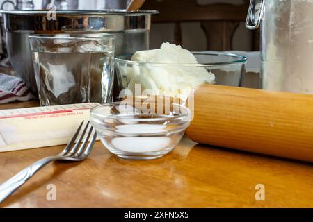 Ingredienti per una torta: Ciotola con ripieno, burro, sale, acqua, grasso per pasticceria, e farina per la crosta. Gli utensili includono una forchetta, un piatto per torte, e. Foto Stock