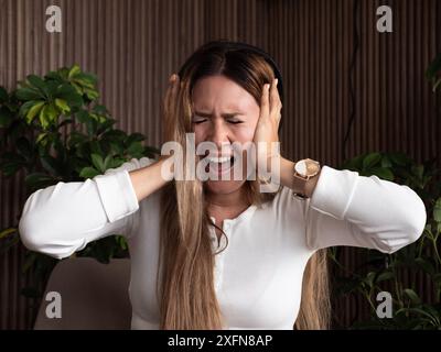 Giovane donna stressata che si copre le orecchie con le mani, avverte forti rumori o mal di testa. Foto Stock