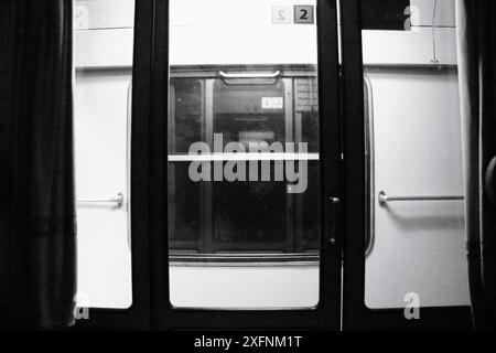 Questa fotografia in bianco e nero cattura la vista dall'interno di un treno, concentrandosi sul finestrino e sul vagone ferroviario adiacente. Foto Stock