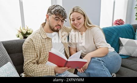 Un uomo e una donna si siedono a stretto contatto leggendo un libro in un salotto accogliente e moderno, suggerendo un momento intimo e rilassato a casa. Foto Stock