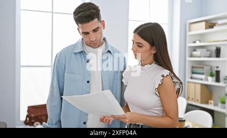 Un uomo e una donna che esaminano un documento insieme in un ambiente d'ufficio moderno, trasmettendo lavoro di squadra e professionalità. Foto Stock