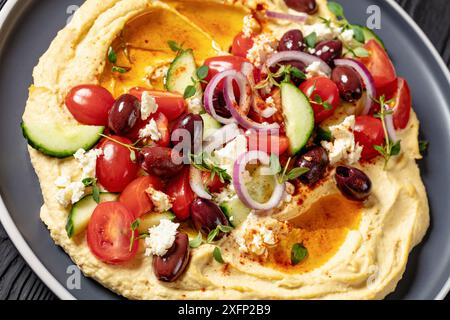 Primo piano di hummus greco carico di cetrioli freschi, olive, pomodori, feta, cipolle rosse e timo sul piatto Foto Stock