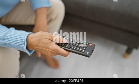 Vista ravvicinata della mano di una donna che tiene in mano un telecomando tv all'interno, simboleggia il tempo libero e la tecnologia in un ambiente domestico. Foto Stock