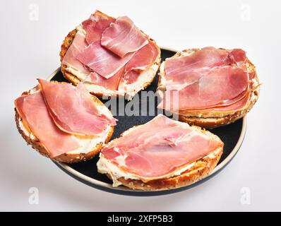 Un piatto di panini a vista appena preparati con prosciutto e formaggio spalmabile su pane multigrano su sfondo bianco. Foto Stock