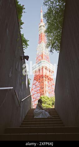 Bellissima donna ispanica con occhiali appollaiati sulle scale, un ritratto della modernità urbana nel famoso punto della torre di tokyo Foto Stock