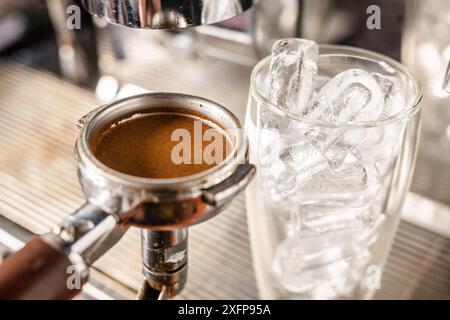 la mano del barista tiene un cono con caffè macinato vicino alla macchina da caffè e prepara il caffè freddo, il barista prepara il latte ghiacciato Foto Stock