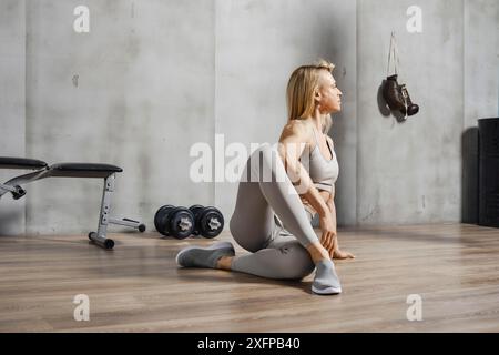 Una donna atleta siede sul pavimento in palestra e fa i crampi in vita Foto Stock