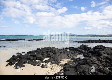 Piccole onde circondano rocce laviche con acqua in riva al mare. Costa di un'isola nell'Oceano Indiano. Alba al mattino, bella luce calda accesa Foto Stock