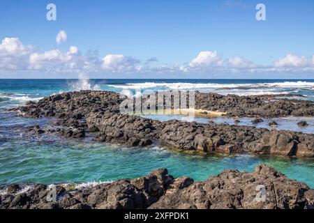 Piccole onde circondano rocce laviche con acqua in riva al mare. Costa di un'isola nell'Oceano Indiano. Alba al mattino, bella luce calda accesa Foto Stock