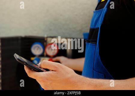 Meccanico esperto che ordina nuovi componenti per il climatizzatore fuori servizio dopo aver terminato la ricerca guasti. Esperto esperto che cerca online su smartphone le parti di ricambio del sistema hvac, primo piano Foto Stock