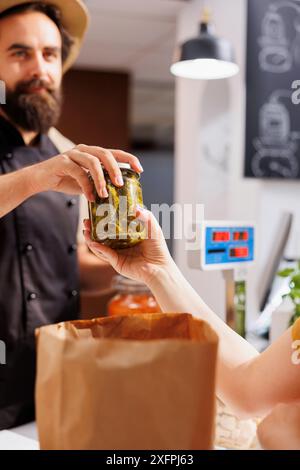 Cliente al banco cassa nel negozio zero rifiuti, che acquista verdure ecologiche di provenienza locale da un negoziante sorridente. Cliente che acquista prodotti alimentari senza pesticidi naturali Foto Stock