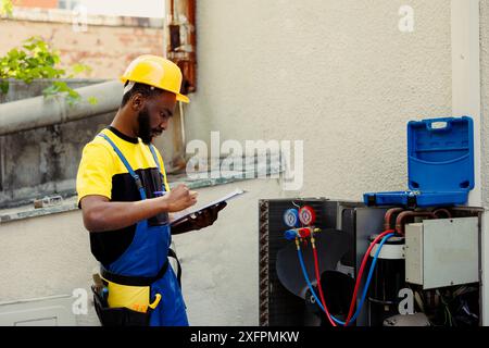 Tecnico addestrato che esegue controlli delle perdite, sostituzioni dei filtri e riparazioni necessarie per evitare guasti gravi. Un tecnico esperto esegue la ricerca guasti del condizionatore d'aria, scrivendo i risultati sulla clipboard Foto Stock