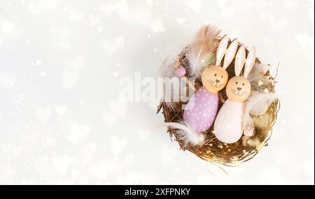 Coniglietto di Pasqua o coniglio seduto accanto a un cesto di vimini pieno di uova colorate, vacanze primaverili Foto Stock