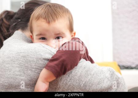 Il bambino è tra le braccia di sua madre e poggia la testa sulle spalle. Concetto di famiglia, maternità e infanzia. Foto Stock