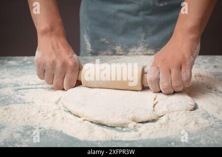 Il panettiere stende l'impasto per pizza, focaccia o pasticceria con il mattarello, prepara gli ingredienti per il cibo e prepara la cottura per le vacanze Foto Stock