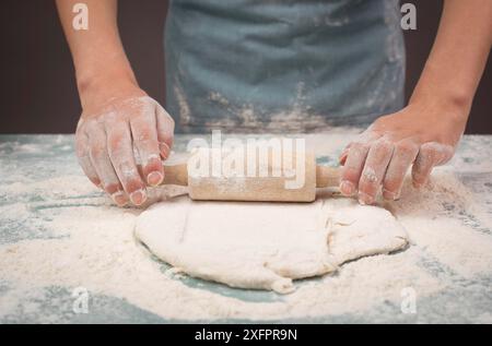 Il panettiere stende l'impasto per pizza, focaccia o pasticceria con il mattarello, prepara gli ingredienti per il cibo e prepara la cottura per le vacanze Foto Stock