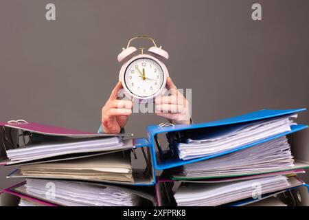 Sveglia accanto a una pila di cartelle di file, esaurimento, stress e sovraccarico, pressione sul lavoro, scadenza Foto Stock