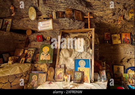 Area dell'altare in una grotta rocciosa, circondata da varie croci e simboli e icone religiose, chiesa rupestre di Agios Nikolaos, Oasis Beach, Kallithea Foto Stock