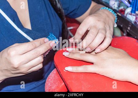 dettaglio delle mani di un manicurista professionista che pulisce le unghie del suo cliente con una piccola spazzola, prima di applicare la lucidatura Foto Stock