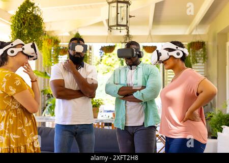 Utilizzando i visori per la realtà virtuale, un gruppo di amici eterogenei si diverte a sperimentare insieme la realtà virtuale Foto Stock