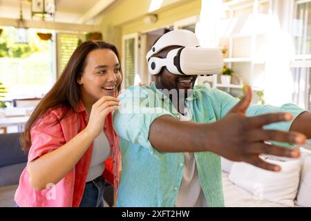 Utilizzando il visore VR, l'uomo esplora il mondo virtuale mentre la donna ride nelle vicinanze Foto Stock