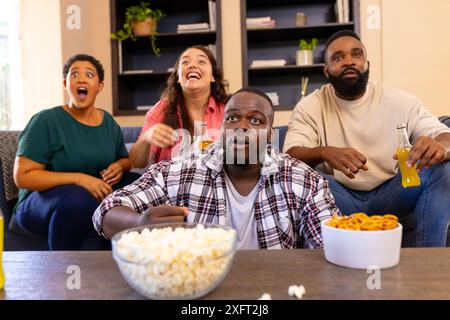 Guardare la TV, un gruppo di amici diversi che gusta spuntini e bevande nel soggiorno Foto Stock