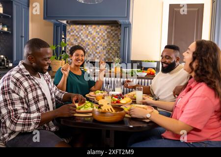 Amici diversi che mangiano insieme, sorridono e ridono intorno al tavolo da pranzo Foto Stock