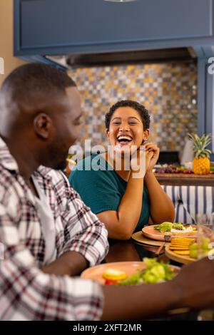Amici diversi che mangiano insieme, ridono e parlano al tavolo da pranzo Foto Stock