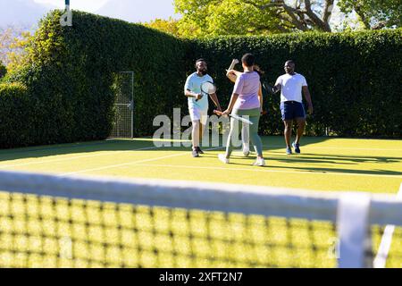 Giocando a tennis, un gruppo di amici diversi si diverte a praticare attività all'aperto nelle giornate di sole Foto Stock