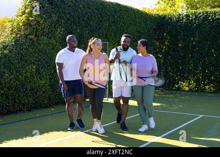 Giocare a tennis, un gruppo di amici che camminano sul campo tenendo racchette e sorridendo Foto Stock