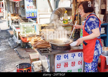 Busan, Corea del Sud - 7 ottobre 2017: Donna coreana che serve piatti caldi alle ciotole presso il caffè di strada nel mercato del pesce di Jagalchi. Foto Stock