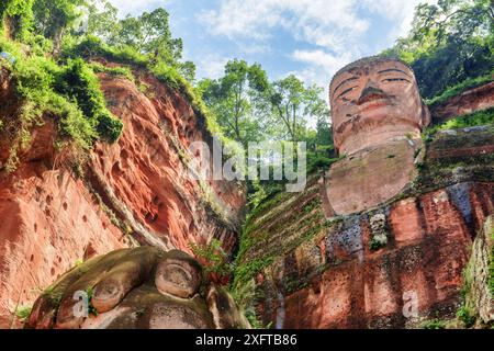 Il Buddha gigante di Leshan sullo sfondo blu del cielo. Vista dal basso nelle giornate di sole. La statua di Buddha in pietra più grande e più alta del mondo. Foto Stock