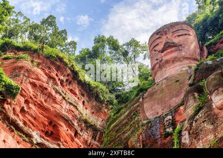 Il Buddha gigante di Leshan sullo sfondo blu del cielo. Vista dal basso nelle giornate di sole. La statua di Buddha in pietra più grande e più alta del mondo. Foto Stock