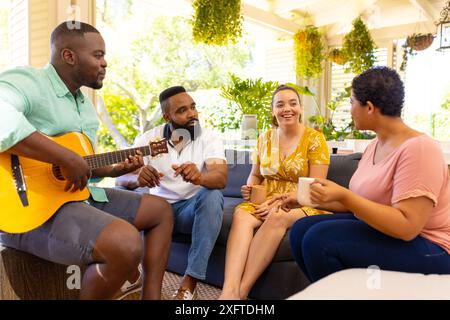 Suonando la chitarra e gustando un caffè, amici diversi che si rilassano insieme sul patio Foto Stock