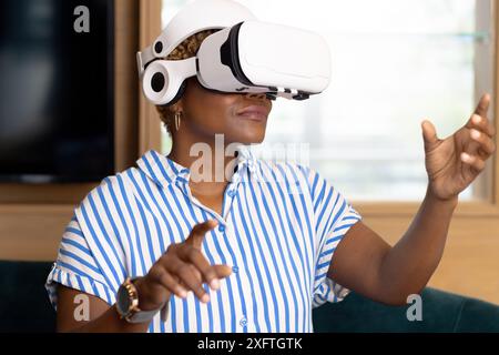 Utilizzando il visore VR, una donna afroamericana che esplora la realtà virtuale con le mani alzate Foto Stock