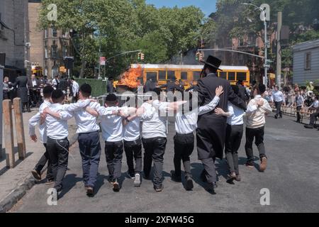 Durante le celebrazioni del Lag Bomer 2024, un rabbino e i suoi studenti ballano in linea verso il fuoco tradizionale. A Brooklyn, New York. Foto Stock