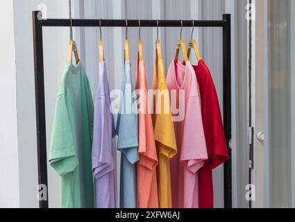 T-shirt multicolore su grucce esposte nel negozio. Abiti sul rack con sfondo bianco. T-shirt in vendita nella boutique. negozio di abbigliamento. Foto Stock