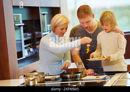 Famiglia in cucina. Tre generazioni. Mangiare sano. Crescita sana. Cucina di pesce e spiedino di vegetali. Foto Stock