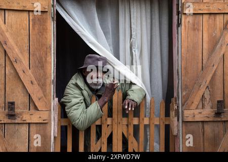 Vecchio che guarda fuori dalla sua casa, villaggio di Andasibe, Madagascar orientale, agosto 2017. Foto Stock