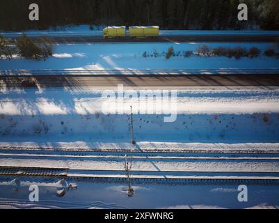 Vista dei droni del camion sull'autostrada tramite i binari della ferrovia in mezzo alla neve Foto Stock