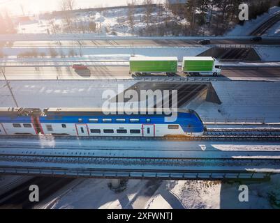 Vista droni di camion e auto sul cavalcavia vicino al treno in mezzo alla neve Foto Stock