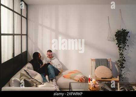 Felice coppia multirazziale che trascorre il tempo libero seduto sul divano nel soggiorno di casa Foto Stock