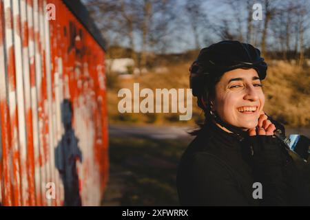 Ciclista sorridente che indossa il casco contro il ferro ondulato Foto Stock