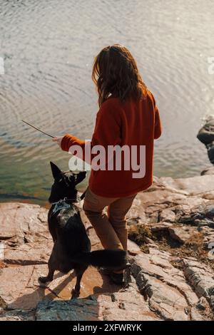 Vista posteriore di una giovane donna con un cane in piedi sulla riva del lago Foto Stock