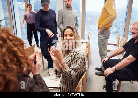 Sorridente giovane donna d'affari applaude mentre siede con i colleghi in ufficio Foto Stock