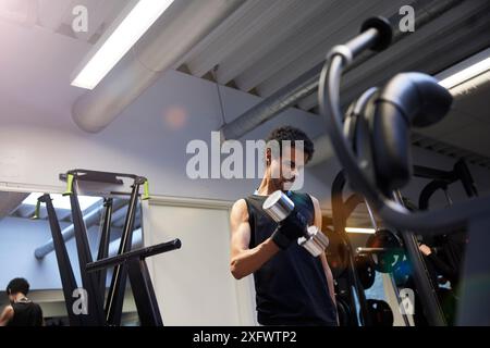 Vista ad angolo basso del giovane determinato che si allena con i manubri in palestra Foto Stock
