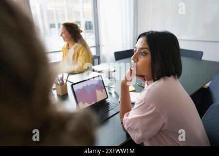 Donna d'affari seria che guarda lontano mentre sedeva sul tavolo in ufficio Foto Stock