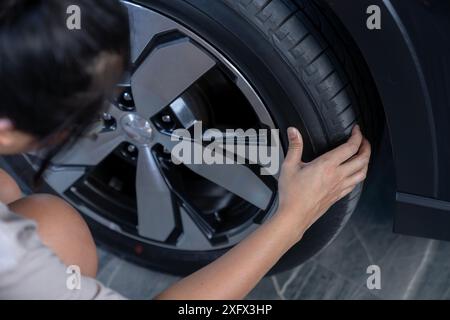 Una giovane donna sta controllando la pressione degli pneumatici dell'auto prima di partire per un viaggio Foto Stock