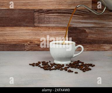 Una tazza di caffè bianca con un flusso di caffè che fuoriesce su uno sfondo in legno Foto Stock